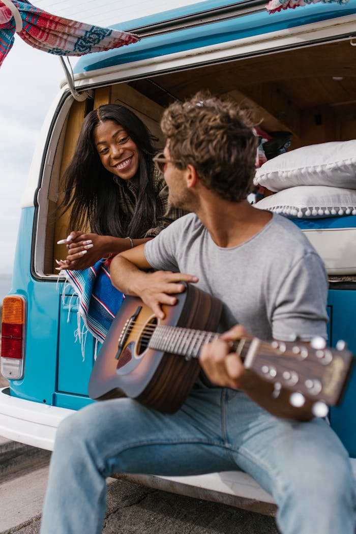 A joyful couple relaxing with a guitar by their van, embracing van life and harmony.